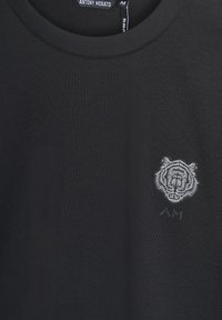 Camiseta negra de manga corta con cuello redondo y un gráfico de cara de tigre gris en el lado izquierdo del pecho, hecha de una tela suave y con un corte ajustado.