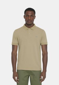 Polo beige con colletto, maniche corte e un piccolo logo blu sul petto; realizzato in cotone morbido.