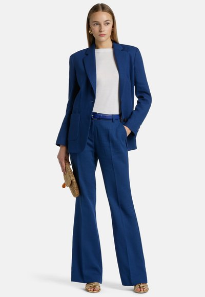 Royal blue tailored blazer and pants set, lightweight fabric, slim fit, pocket details, paired with gold-accents sandals and a woven bag.