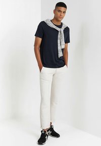 Tamsiai mėlynas marškinėliai, ant pečių užmestas pilkšvas megztinis, derinamas su šviesių kreminių siaurų kelnių ir juodų sportinių batelių pora.