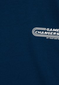 Granatowy materiał z białym logo tekstowym "Game Changers by Bad Boys" na wysokości klatki piersiowej.