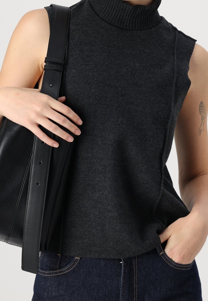 Haut sans manches col roulé gris foncé en tissu doux, avec un col côtelé. Associé à un grand sac en cuir noir et un jean bleu.