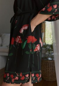Zwart bloemenjurk met rode rozen, met een gladde stof, korte mouwen, zijzak, en een strik taille, afgewerkt met een groene rand.