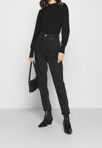 Czarny sweter z dzianiny z bufiastymi rękawami oraz dekoracyjnymi guzikami na ramieniu. W zestawie z czarnymi dżinsami z wysokim stanem i botkami za kostkę.