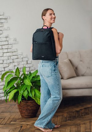 Schwarzer Rucksack aus Nylon mit frontalem Fach, Obergriff und verstellbaren Trägern, getragen von einer Person in legerer Kleidung.