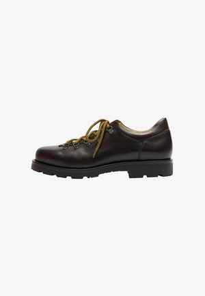 Zapato de cuero marrón con una textura suave, puntera redonda y cordones amarillos en contraste. Suela de goma negra gruesa con un patrón texturizado.