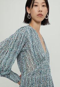 Rochie cu imprimeu, cu decolteu în V, mâneci lungi și talie strânsă. Materialul prezintă un design ondulat în nuanțe de albastru, verde și roșu.