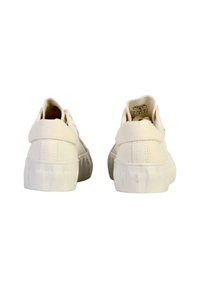 Baskets en toile blanches avec une semelle en caoutchouc texturé, un dos arrondi et un col de cheville rembourré. Design minimaliste sans marque visible.