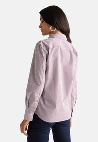 Camicia a righe bianca e rosso scuro, con maniche lunghe, bottoni ai polsini e colletto classico. La vista posteriore evidenzia i dettagli della spalla.