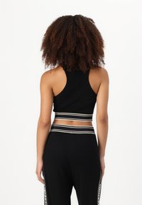 Melnā īsā sporta tank topa ar gludu tekstūru, kuram ir plats, kontrastējošs svītrains josta un racerback dizains, apvienots ar melnajiem sporta biksēm.