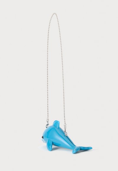 Petit sac bleu en forme de dauphin avec une bandoulière en chaîne à billes argentées sur un fond blanc uni.