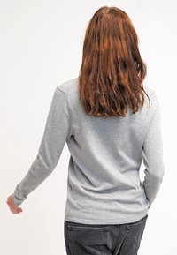 Pull gris à manches longues en tissu doux, avec un col rond et des poignets côtelés. La vue de dos montre un design lisse et ajusté.