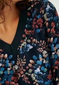 Navy top w kwiatowym wzorem z dekoltem w kształcie V, z niebieskimi i rdzawymi akcentami na miękkiej, strukturalnej powierzchni.