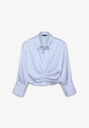 Camicia corta in raso bianco con colletto a punta, chiusura con bottoni e maniche lunghe. Presenta un dettaglio di tessuto arricciato sotto i bottoni.