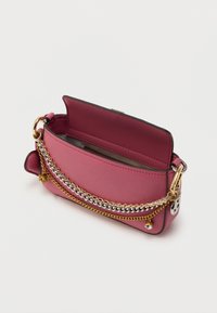 Ροζ δερμάτινη τσάντα χειρός με χρυσές και ασημένιες αλυσίδες, ανοιχτό καπάκι που αποκαλύπτει το εσωτερικό και διακοσμητικά γούρια στο λουρί πάνω σε λευκό φόντο.