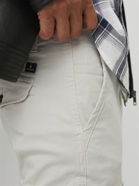 Light beige pants with a soft texture, featuring side pockets and stitching details. A black zipper jacket is partially visible.