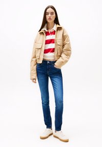 Beige kort jacka, röd- och vitrandig pikétröja, blåa smala jeans och vita sneakers med beiga sulor. Enkel design och avslappnad passform.