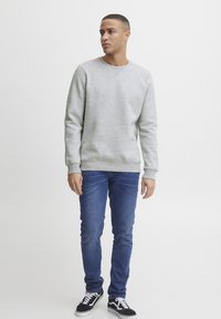 Gray sweatshirt with long sleeves, ribbed cuffs and hem, paired with dark blue jeans and black sneakers with white accents.