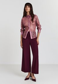 Lace Button-up-Bluse in Pink mit satinierten Manschetten, kombiniert mit weit geschnittenen bordeauxroten Hosen und dunkelroten High Heels, überzeugt durch einen entspannten Schnitt.