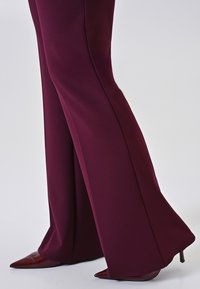 Bordeauxkleurige broek met een flared ontwerp, gemaakt van een gladde stof, gecombineerd met puntige rode lakleren hakken. Op maat gemaakte benen met een scherpe silhouet.