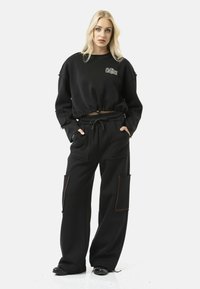 Zwarte cropped sweatshirt met logo en zwarte sweatpants met een losse pasvorm, voorzien van cargozakken en contrasterende stikseldetails.