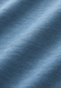 Țesătură tricotată albastru deschis, cu textură fină, uniformă și pliuri delicate care creează umbre subtile și profunzime.