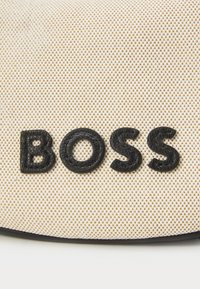 Black textured lettering "BOSS" on a beige and gold patterned fabric background, featuring a smooth, dark edge around the design.