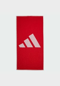 Toalla de algodón roja con un gran diseño de tres rayas blancas, de forma rectangular y con una superficie texturizada. Los bordes están terminados con una costura en contraste.