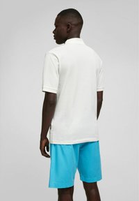 Witte korte mouwen polo-shirt gemaakt van textielstof, gecombineerd met lichtblauwe shorts. Heeft een kraag en een zijsplit voor extra comfort.