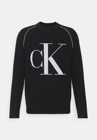Czarny sweter z dużym, białym logo "CK" na przodzie. Okrągły dekolt, długie rękawy oraz kontrastowe szwy na ramionach.
