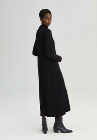 Mustapintainen ribbed midi-mekko, jossa on pitkät hihat ja korkea kaulus. Yhdistetty mustiin nilkkureihin, joissa on paksu korko. Yksinkertainen, elegantti siluetti.