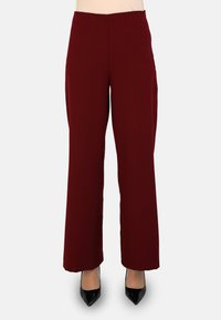Pantalones anchos burdeos con una textura suave, cintura alta y bolsillos laterales, combinados con tacones negros de punta.