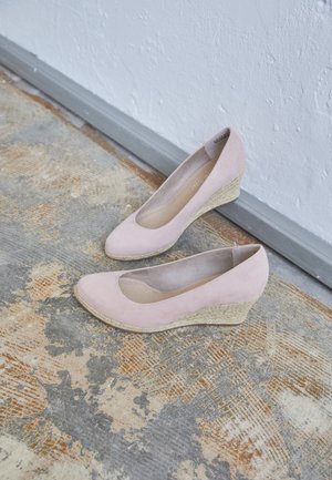 Wedge-Schuhe aus weichem, rosa Wildleder mit runder Zehenpartie, strukturiertem Jutefaser-ähnlichem Absatz und glattem Innenfutter. Auf einer gemusterten grau-braunen Oberfläche platziert.