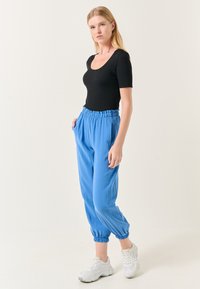 Zwarte ribbelige top met korte mouwen, gecombineerd met lichtblauwe joggerbroeken met elastische taille, voorzien van elastische boorden en zijzakken.