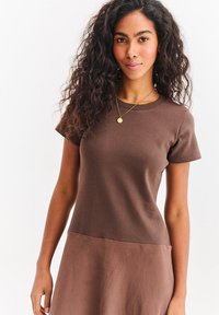 Brązowa prążkowana bluzka z krótkim rękawem z gładką dolną częścią, z okrągłym dekoltem i luźnym krojem. Bez widocznych wzorów i elementów metalowych.