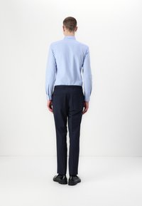 Lichtblauw overhemd met lange mouwen en een kraag, marineblauwe broek en zwarte schoenen, gezien vanaf de achterkant tegen een witte achtergrond.