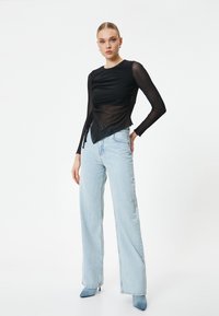 Top negro de manga larga con diseño fruncido y tejido transparente, combinado con jeans de pierna ancha color azul claro y tacones de punta en azul a juego.