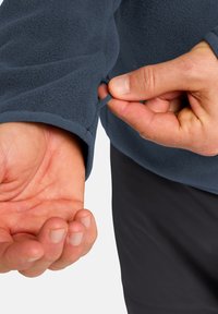 Pullover in pile con tessuto navy testurizzato; presenta un anello per il pollice nascosto all'interno del polsino della manica per una vestibilità sicura; primo piano di una mano che lo regola.