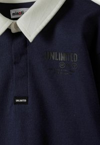 Granatowa koszulka polo z kontrastowym białym kołnierzykiem. Z przodu znajduje się nadrukowane na czarno logo "UNLIMITED", wykonana z miękkiej bawełnianej tkaniny.
