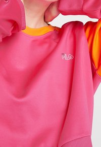 Rosa Sweatshirt mit gerippten Bündchen, orangefarbenem Kragen und einem kontrastierenden orangenen Design an den Ärmeln. Fila-Logo in Weiß gestickt.