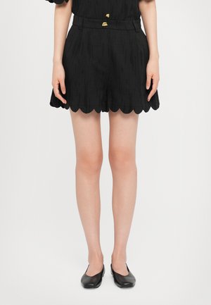 Pantaloni corti neri a scallop in un tessuto testurizzato, con una vita aderente caratterizzata da dettagli in oro. Abbinati a scarpe nere basse.