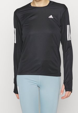Osoba ubrana w czarną, długorękawową sportową koszulkę Adidas z białymi paskami na rękawach oraz jasnoniebieskie legginsy sportowe.