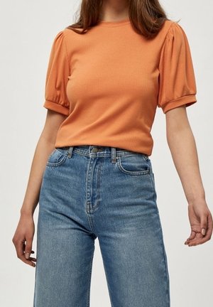 Pomarańczowy prążkowany top z krótkimi bufkami, w połączeniu z jasnoniebieskimi dżinsami z wysokim stanem, wyposażonymi w klasyczny design z pięcioma kieszeniami.