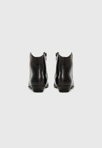 Bottines en cuir noir avec une finition lisse, un petit talon empilé, des zips sur le côté et des détails de couture subtils à l'arrière.