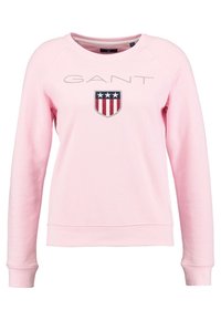 Felpa GANT di colore rosa chiaro con collo rotondo, maniche lunghe e un logo con design a scudo in blu navy e rosso con stelle bianche.