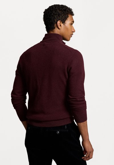 Pull en tricot bourgogne avec un col haut et des manches longues, présentant une finition texturée. Associé à un pantalon noir. Modèle vu de dos.