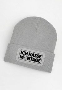 Gray knit beanie with a folded cuff featuring a rectangular patch. The patch has the text “ICH HASSE MONTAGE” and a cat graphic in black.