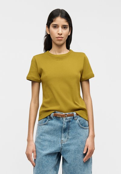 T-shirt vert olive à manches courtes avec col côtelé et petit logo, associé à un jean en denim bleu clair taille haute.