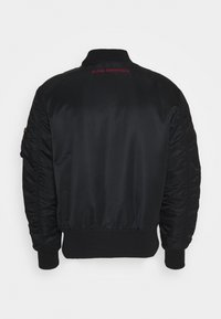 Zwarte bomberjack met een gladde satijnen afwerking. Voorzien van ribgebreide manchetten en tailleband, gewatteerde mouwen en rode "ALPHA INDUSTRIES" tekst op de rug.