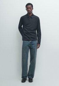 Czarna koszulka polo z długim rękawem, luźny krój, zestawiona z luźnymi niebieskimi dżinsami. Czarny obuwie dopełnia strój. Prosty design, bez wzorów.